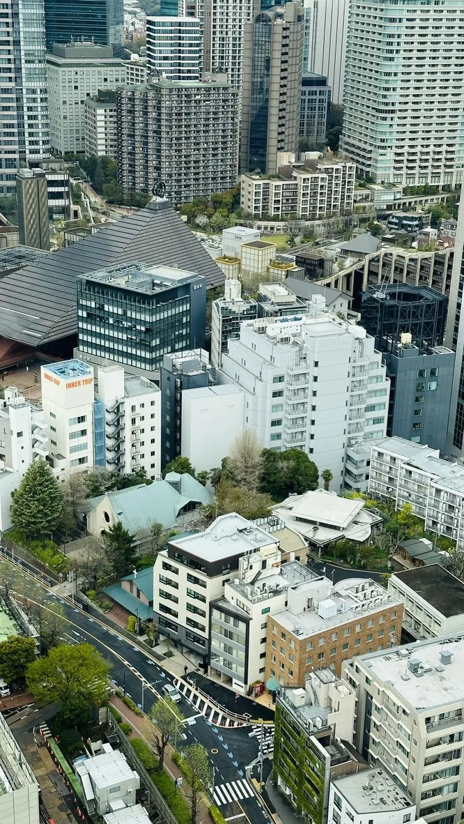 A high-angle view of a bustling urban cityscape, featuring a mix of modern skyscrapers and low-rise buildings. The image shows a variety of architectural styles, green spaces, and busy streets, highlighting the contrast between nature and city life.