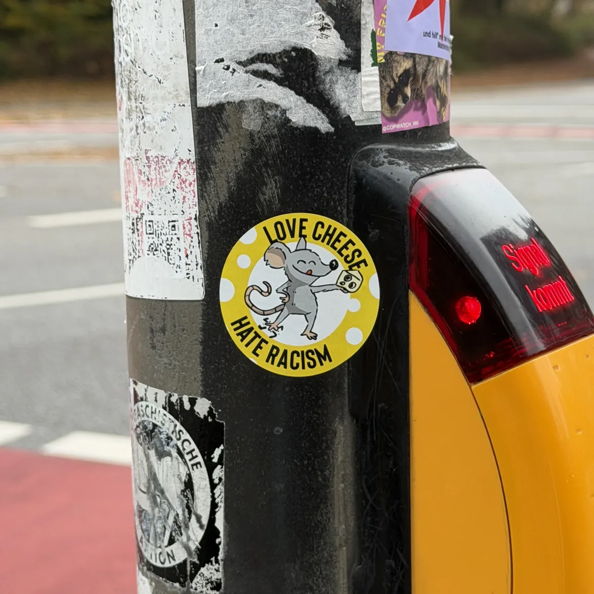 A sticker on a street pole features a cartoon character holding cheese, with the text 