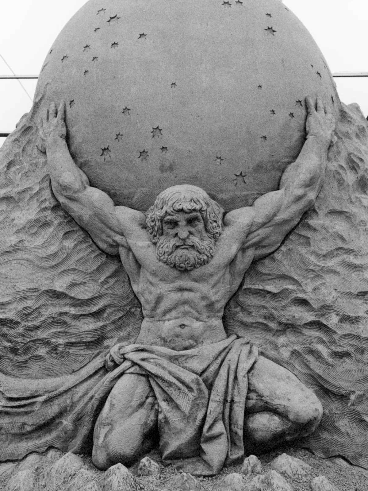 A muscular figure representing Atlas kneels with a large globe on his shoulders, surrounded by stylized waves and stars. The sculpture is detailed, showcasing the figure's flowing hair, beard, and powerful physique.