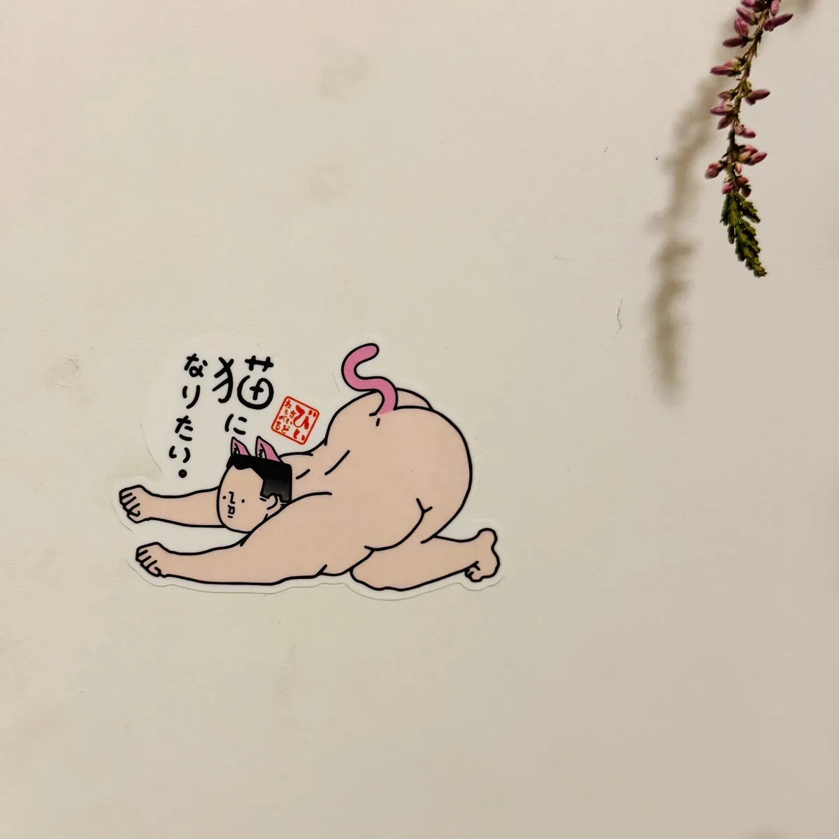 A cartoon sticker depicting a playful hybrid character, combining a naked human body with cat features, including ears and a tail, stretching on a white background. A small Japanese text is visible near the character.