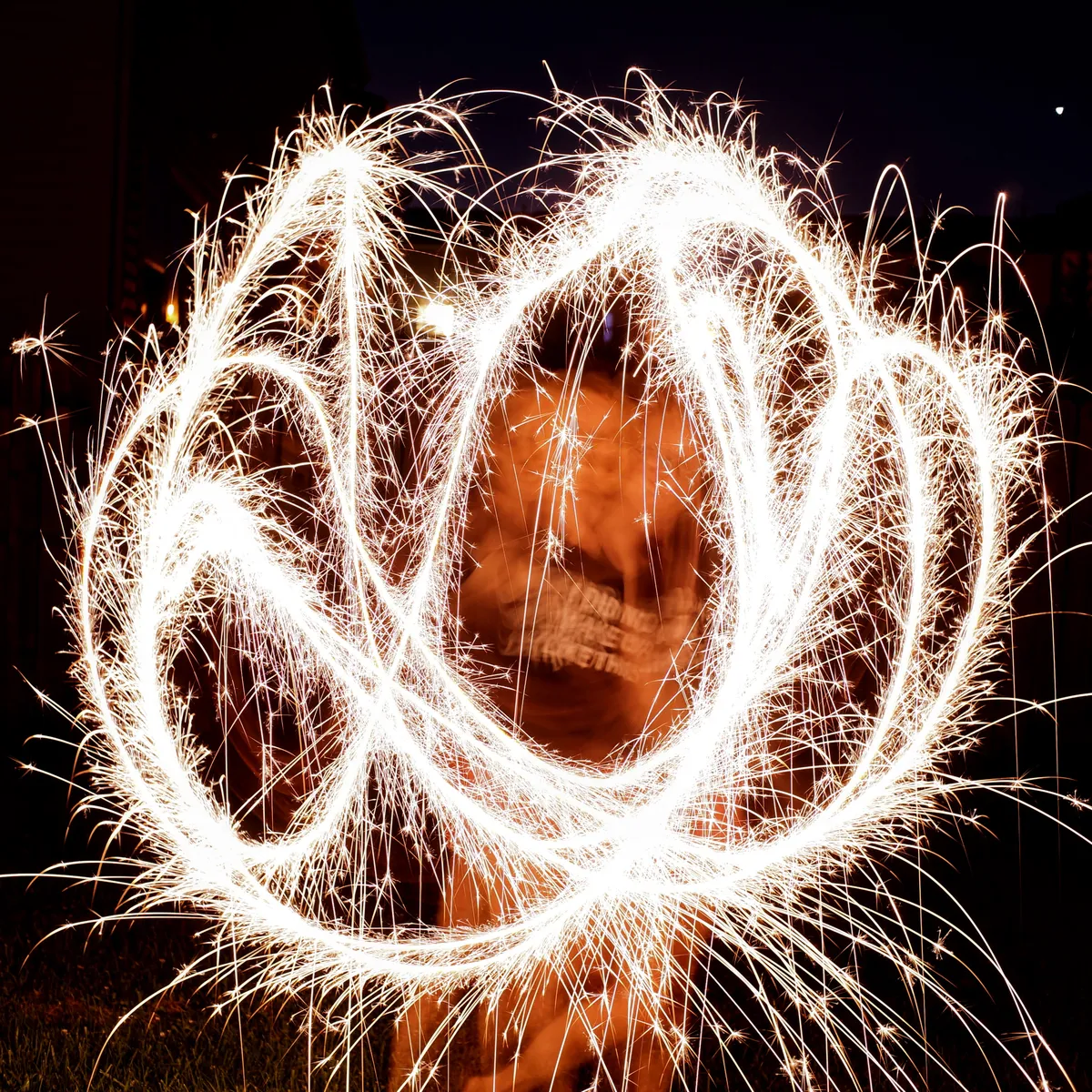 A long exposure photo of my wife swinging around a sparkler in the dark. There's a messy streak of yellow and white sparks surrounding her.