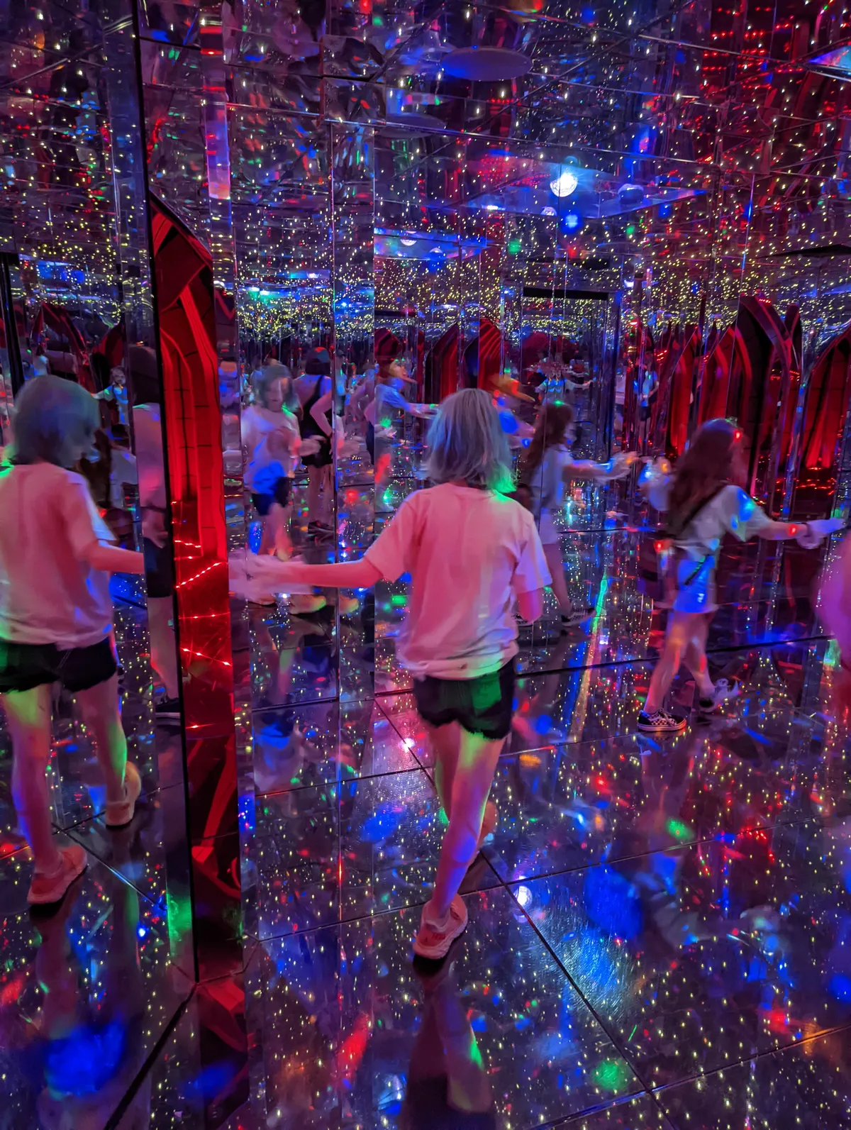 my daughter walking through a colorfully lit hallway of mirrors