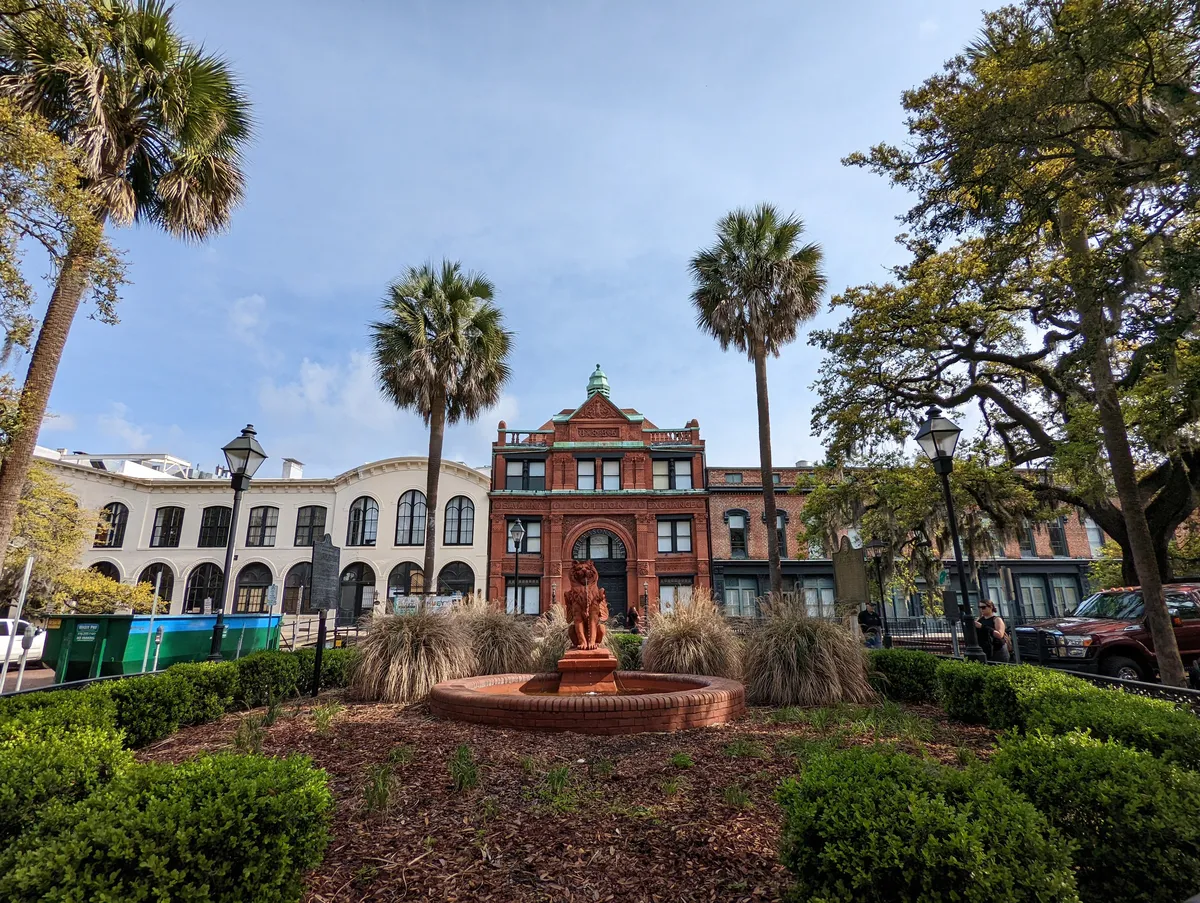 an ultra wide photo of Solomon's Lodge in Savannah, GA surrounded by palm trees and oak trees, a lion water fountain in front