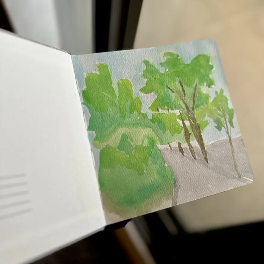 handheld square sketchbook watercolour showing green trees and a light grey simple path