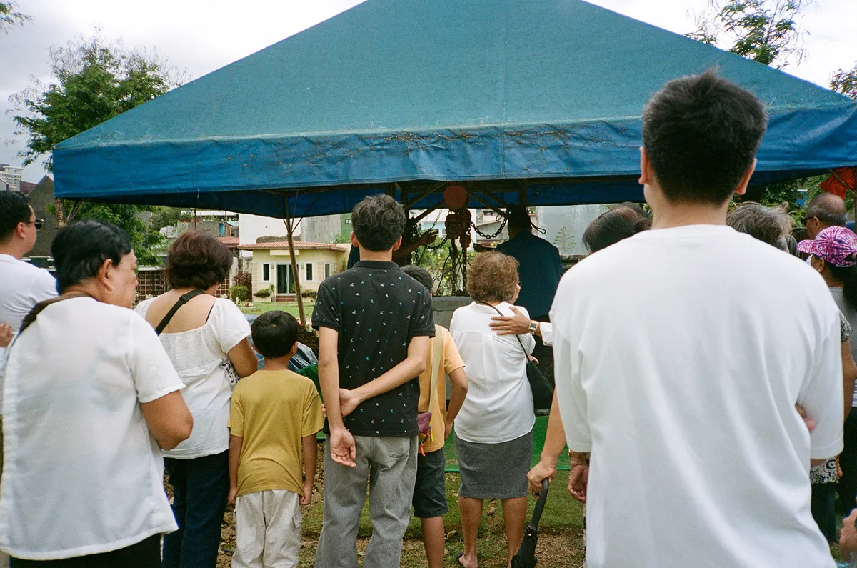 a film photo of my family watching over my Lolo's coffin being lowered to the ground at the funeral, taken behind them