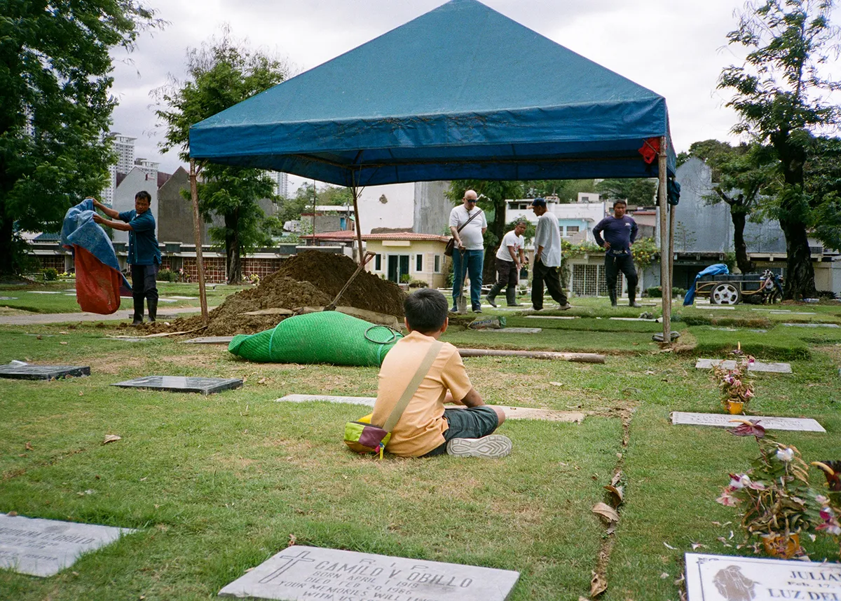 a film photo of my young nephew sitting on the ground, watching the burial