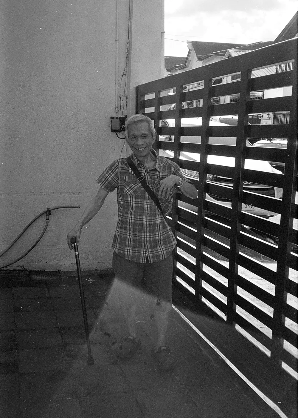 a black and white film photo of my Lolo laughing while holding his walking stick in the garage of our house