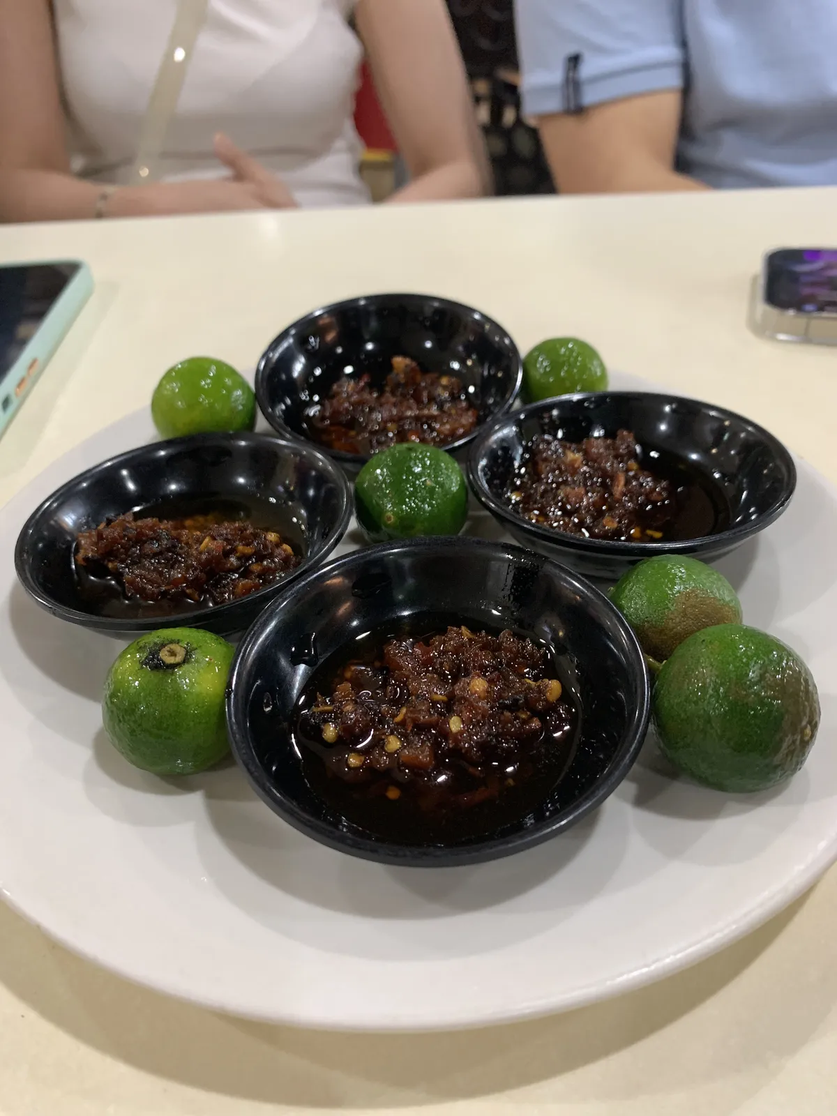 A plate with 4 soy dishes containing chili garlic dip. 6 pieces of calamansi are on the plate as well.