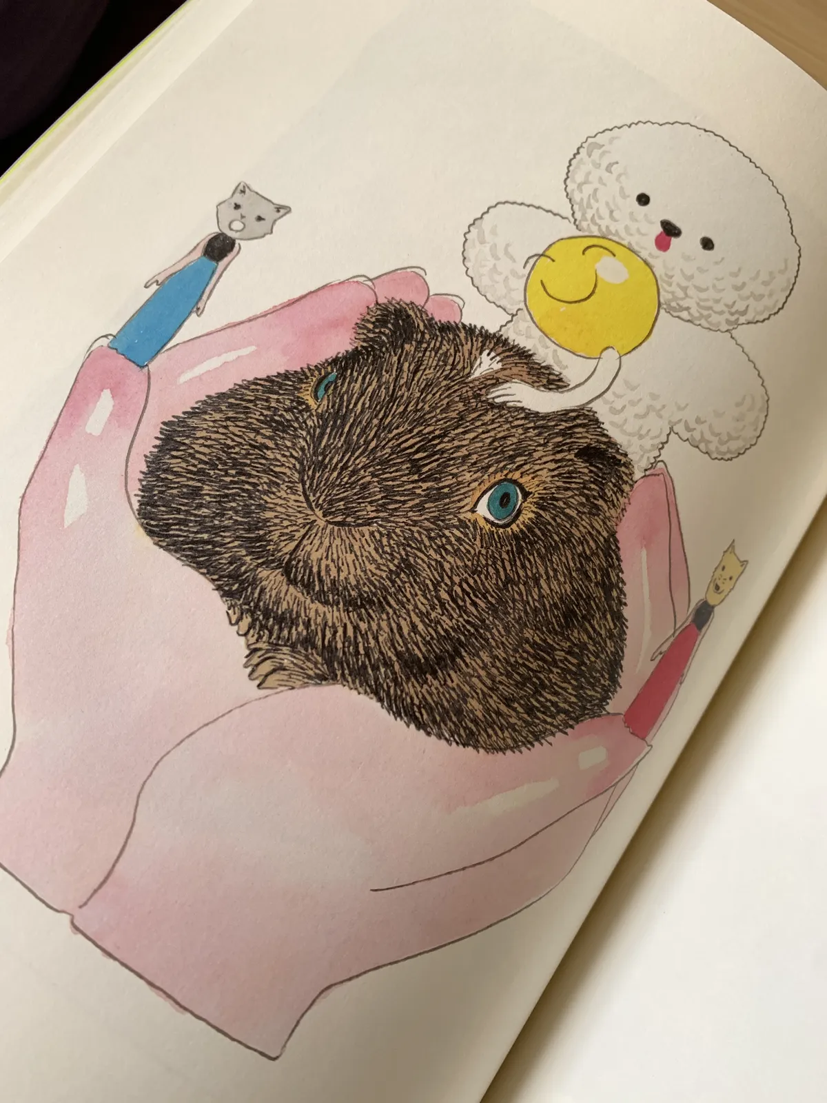 A page of a book with an artwork of a fat guinea pig resting on the pale palm of someone's hands. There is a tiny cat-headed lady and a dog-headed lady standing on each thumb, wearing identical plain dresses. A fluffy white creature resembling a cotton ball stands on top of the guinea pig with a lollipop-like creature, with its spherical yellow head smiling and its stick body turning into a hand and patting the guinea pig's head.