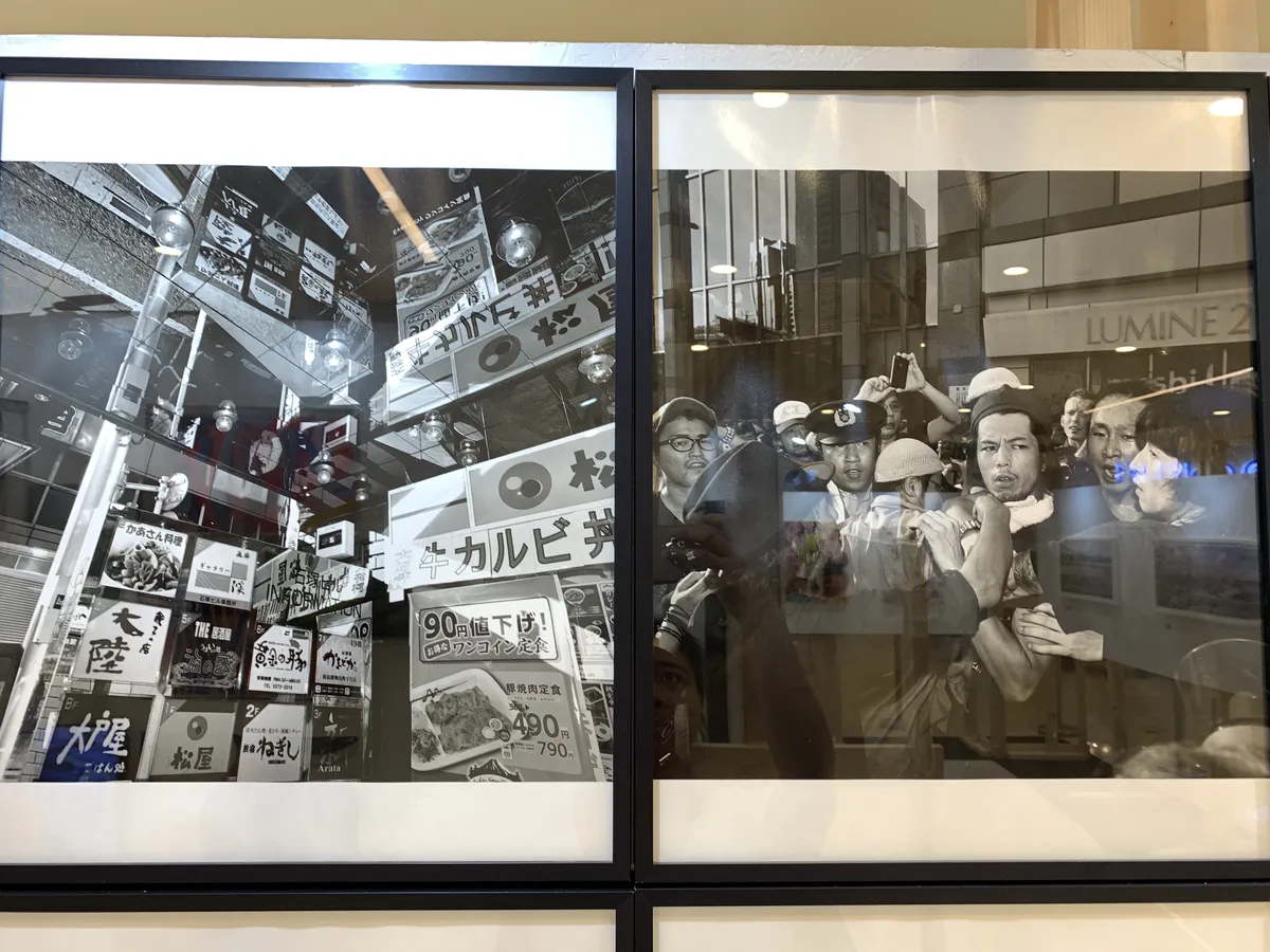 Two framed black and white photographs of street scenes, one is an array of logo signages and the other is a huddled group of men and police in a possible fight.