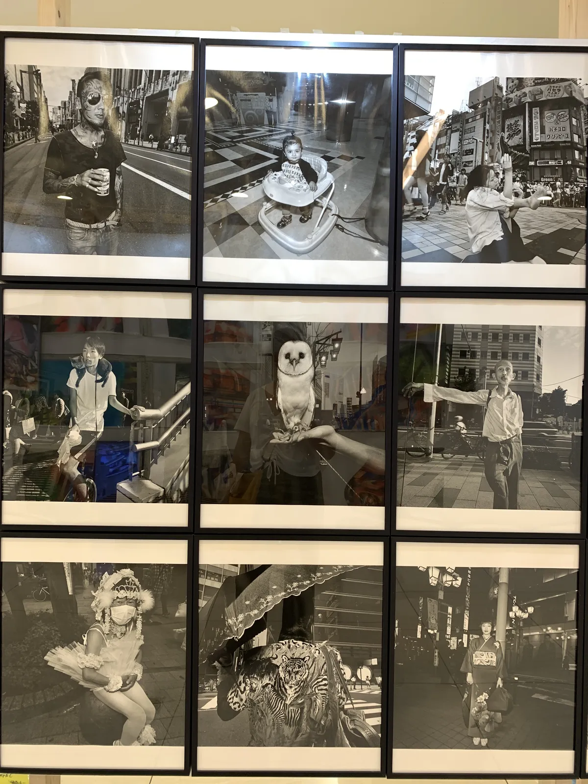 A wall of black-and-white framed photos of street scenes, mostly portraits of people in public.