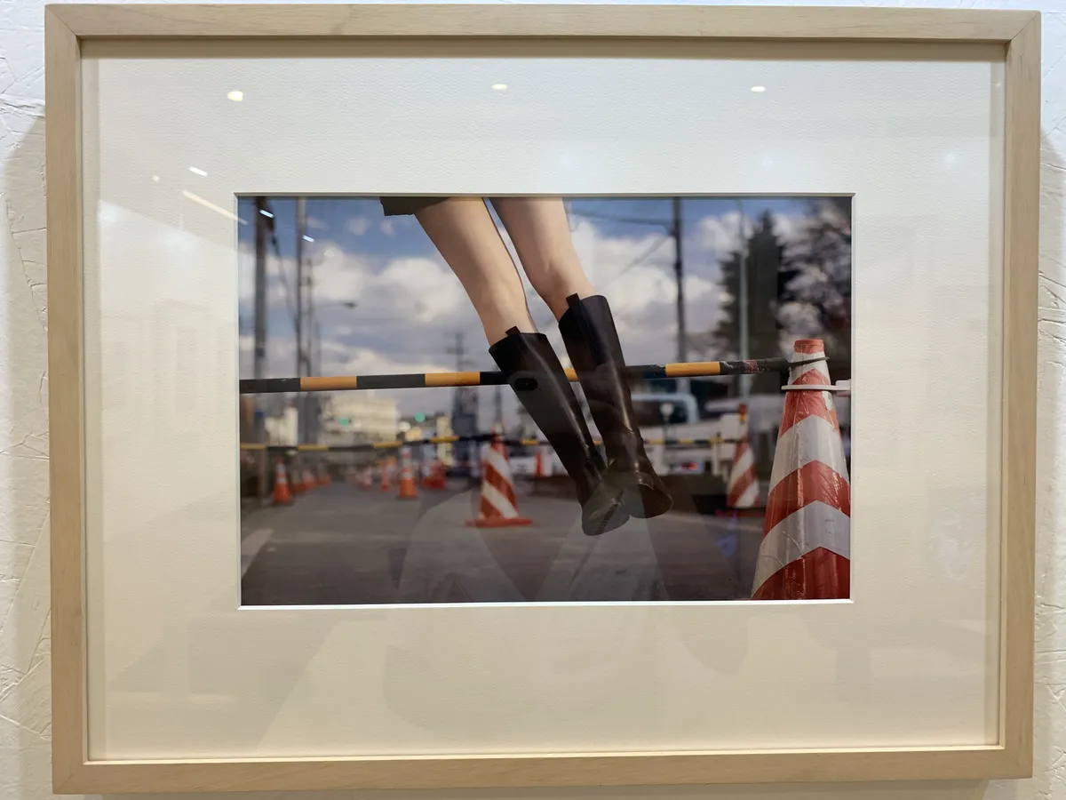 A pair of legs wearing knee-high boots is levitating off the ground, positioned diagonally across the frame. In front of her are several safety barricades and cones.