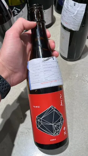 Sake bottle with bright red label and a black prism looking logo printed on it.