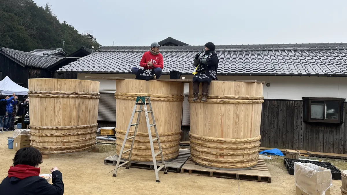 Kanako-san from Yamakawa Jozo Brewery (right) interviewing one of the carpenters (left) teaching how to make Kioke while sitting atop of two new barrels made just before the summit.