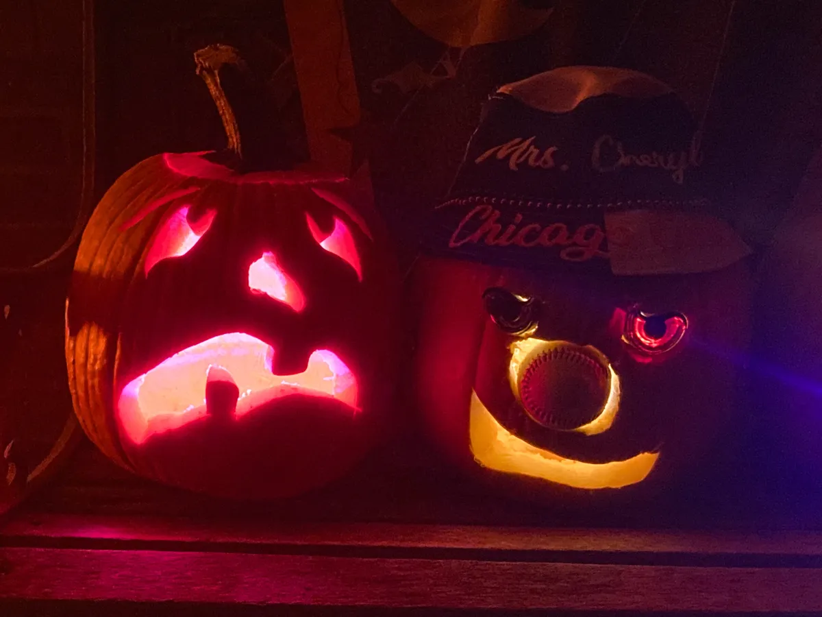 A pumpkin with a silly monster face, next to a pumpkin wearing a Chicago Cubs bucket hat and with a baseball in its nose