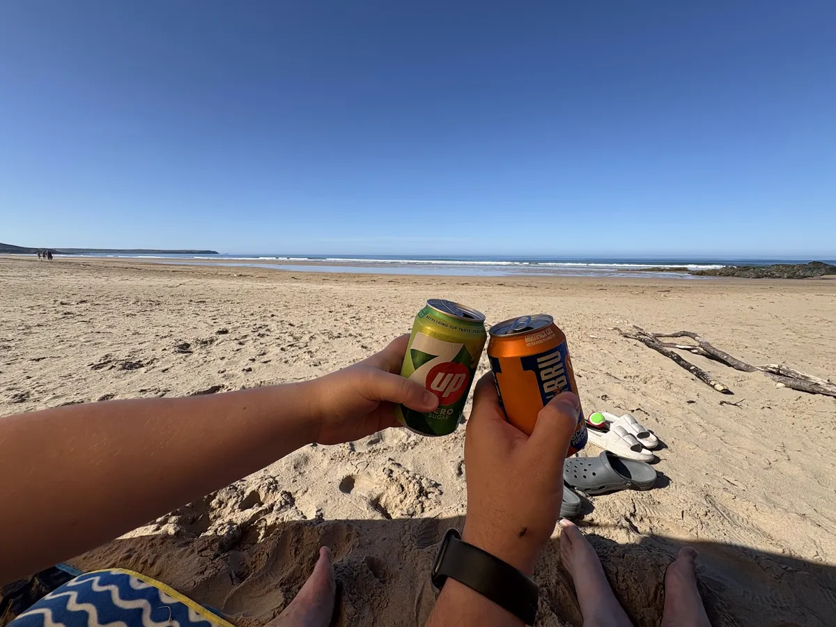 Two people holding cans of drink on a sandy beach