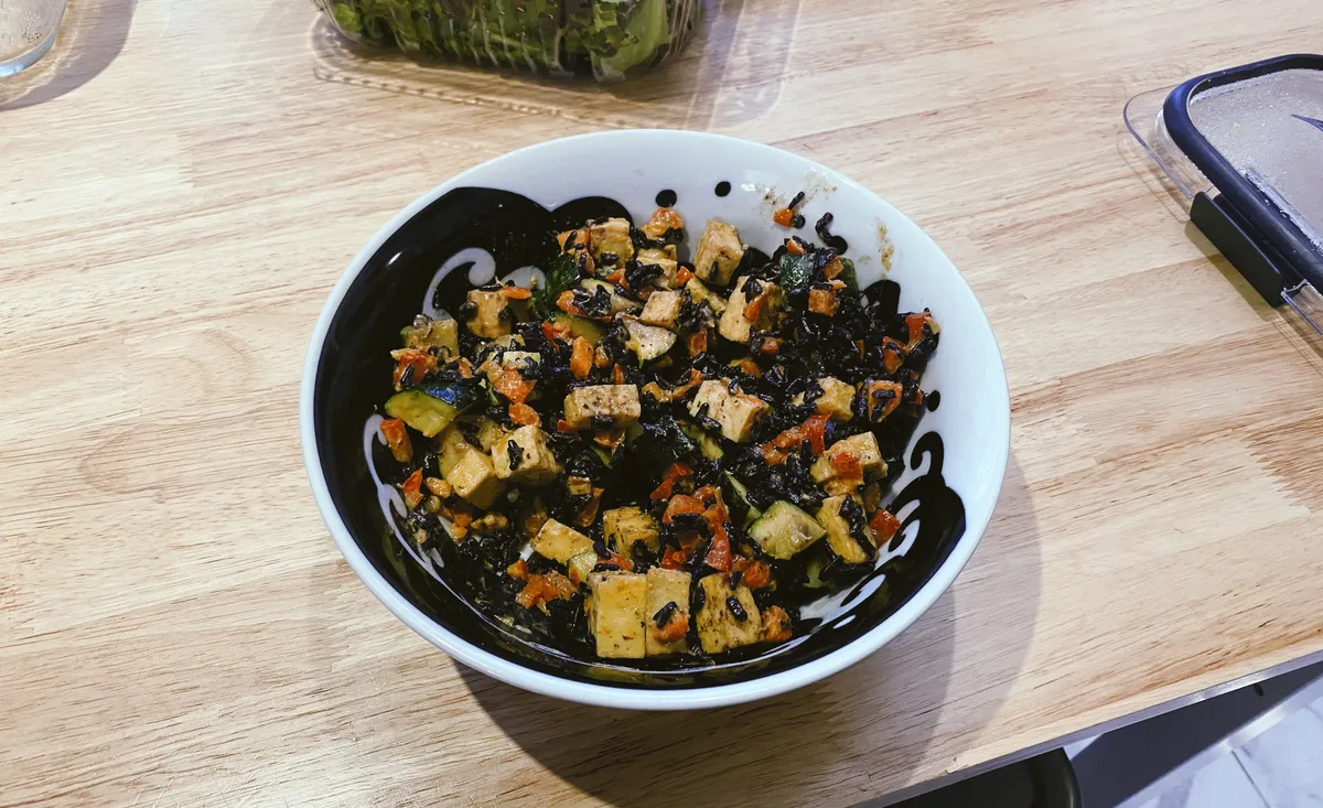 A tofu bowl with zucchini, red bell pepper, and black rice