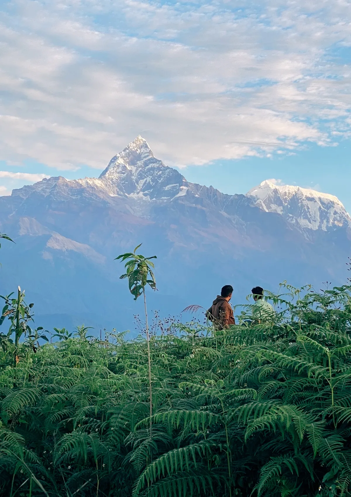 The view of the snow peak of the Himalayan mountains with two people standing in front of it