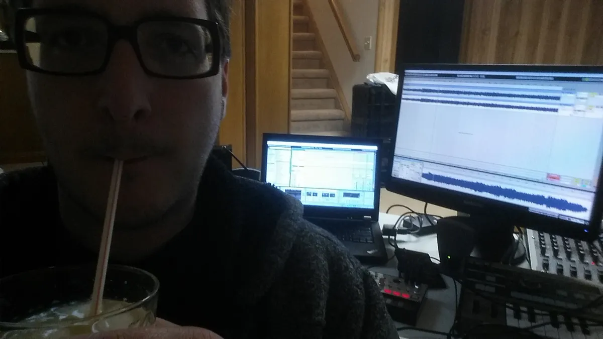 A person sipping a drink. A music workstation is behind him