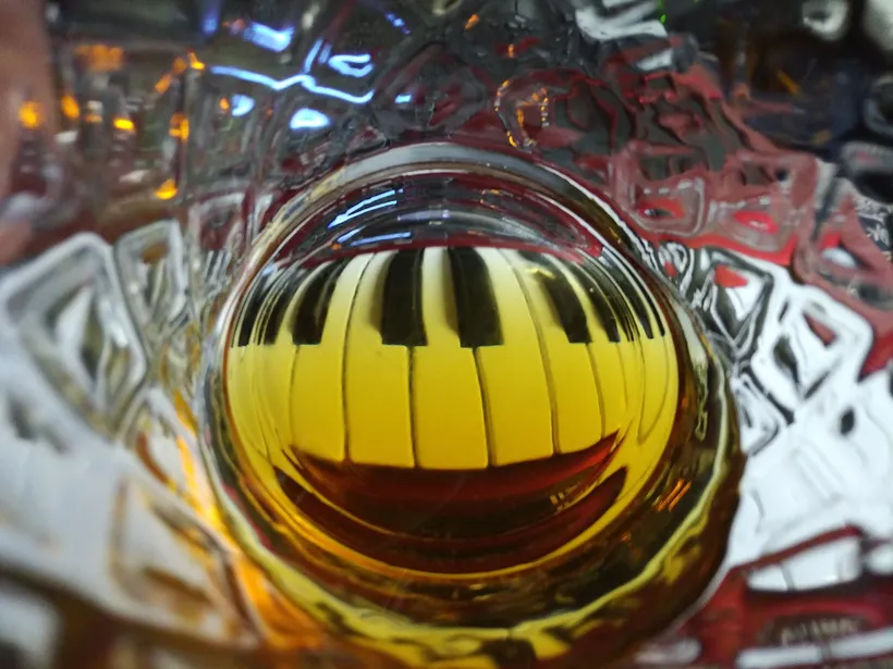 A piano keyboard, viewed through a highball glass with whisky in it.