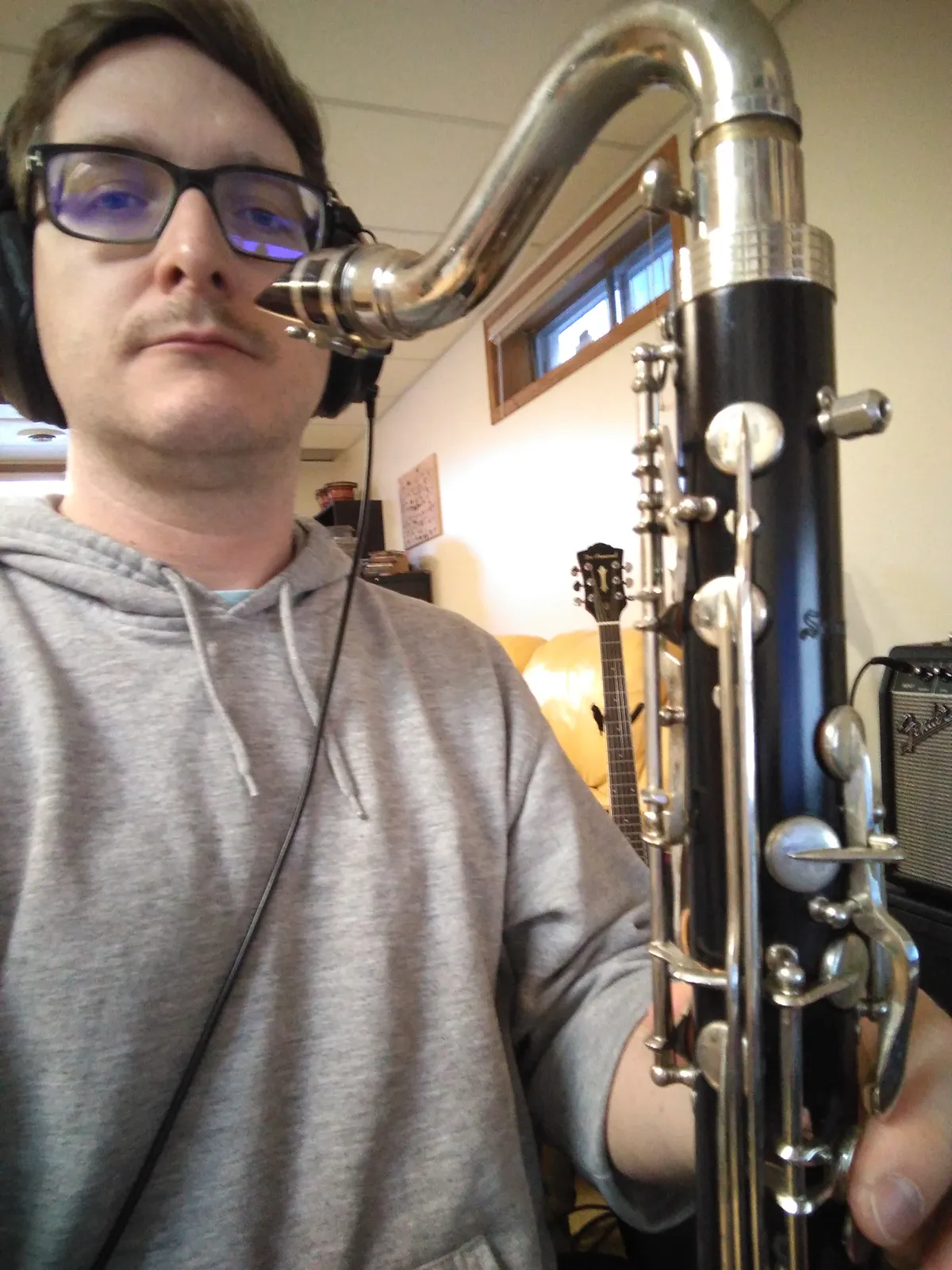 A person holding a bass clarinet and wearing headphones