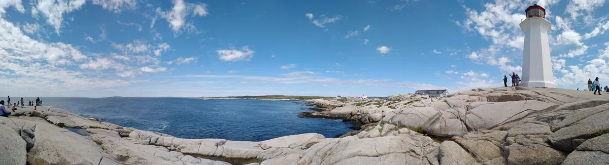 A panoramic view of the ocean, rocks, people and the lighthouse at Peggy's Cove, Nova Scotia
