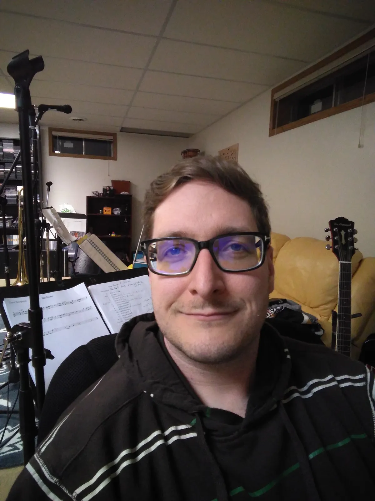 selfie of a person with sheet music and a guitar in the background