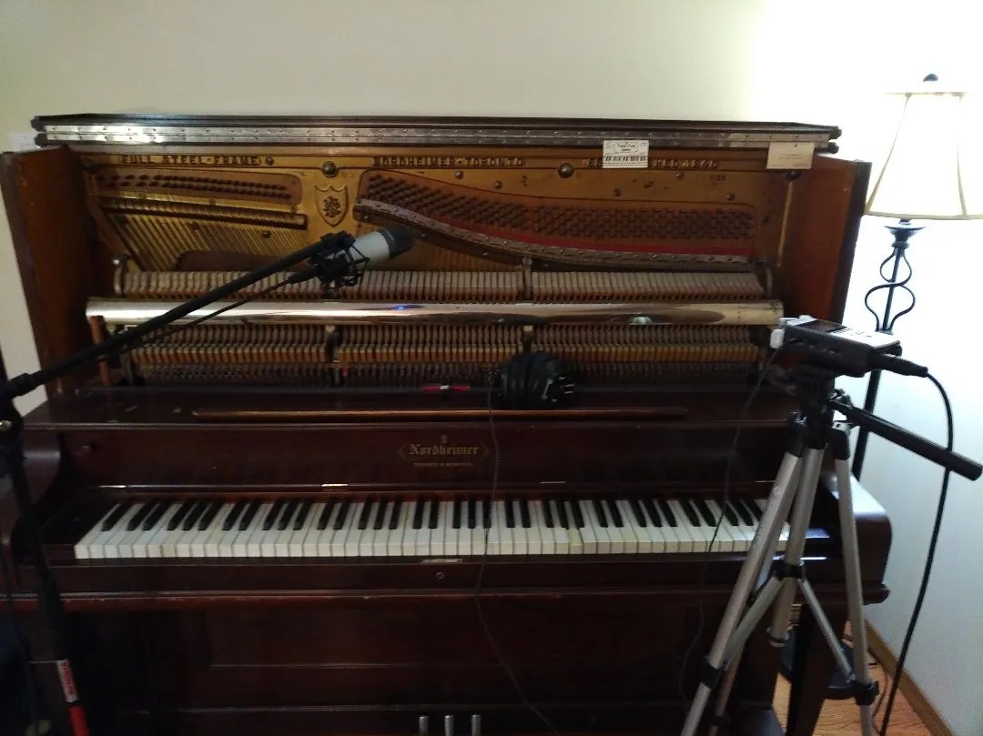 An upright piano with the cover off and microphones on stands pointing towards it