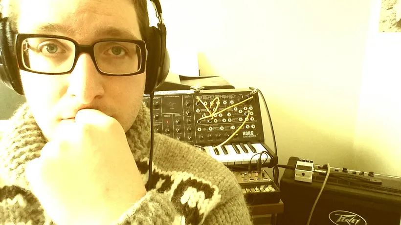 A person wearing headphones. A synthesiser can be seen in the background.