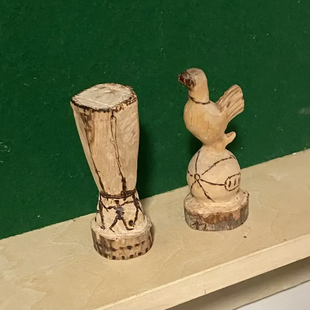 Miniature wooden Europa League Trophy on a shelf next to a miniature wooden Tottenham Hotspur cockerel against a dark green background.