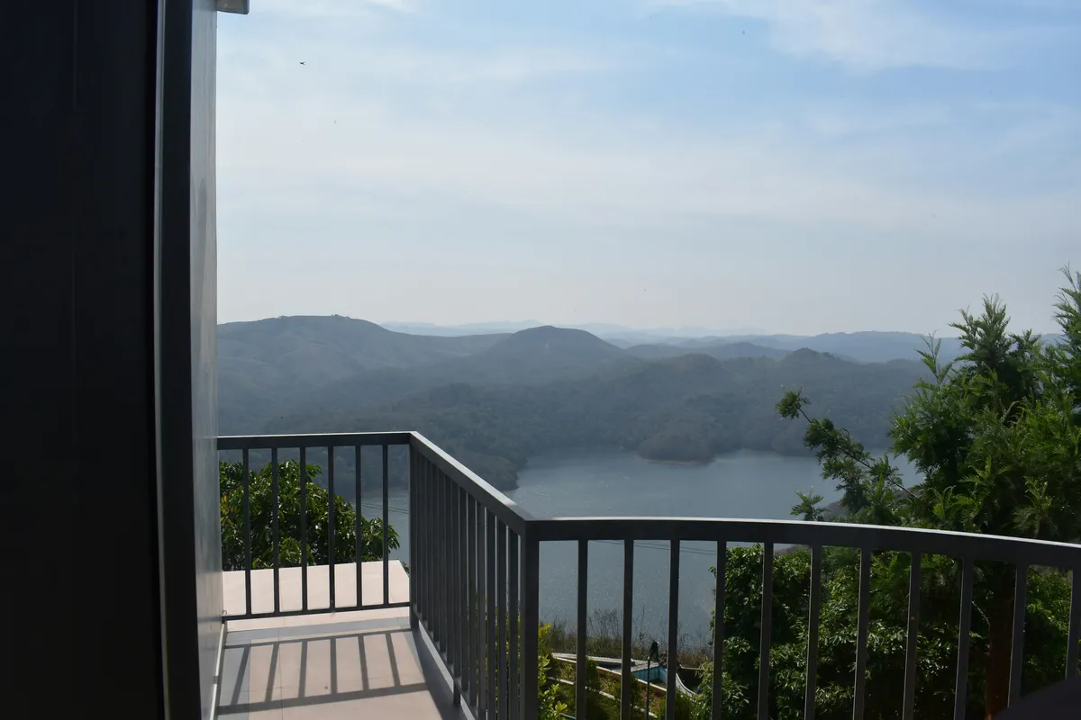 Balcony overlooking a body of water with forested hills under hazy blue skies.