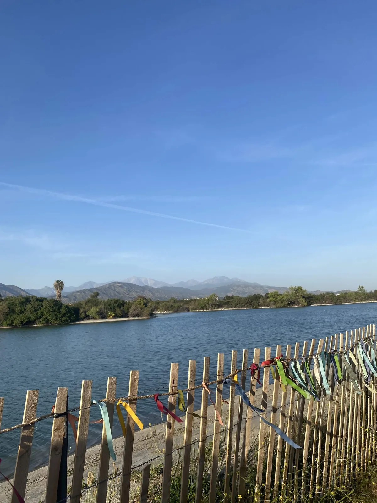 Photo of a lake with color flags decorated on the fence. Mountains and trees in the distance