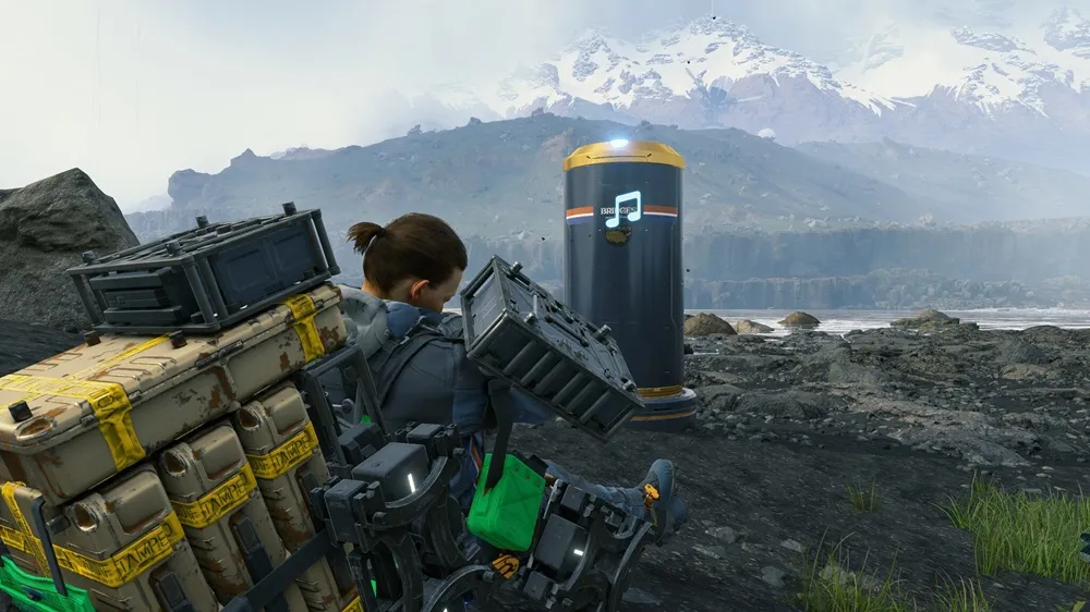a man sitting on the ground with packages on his back, resting in front of a speaker playing music with mountains in the distance