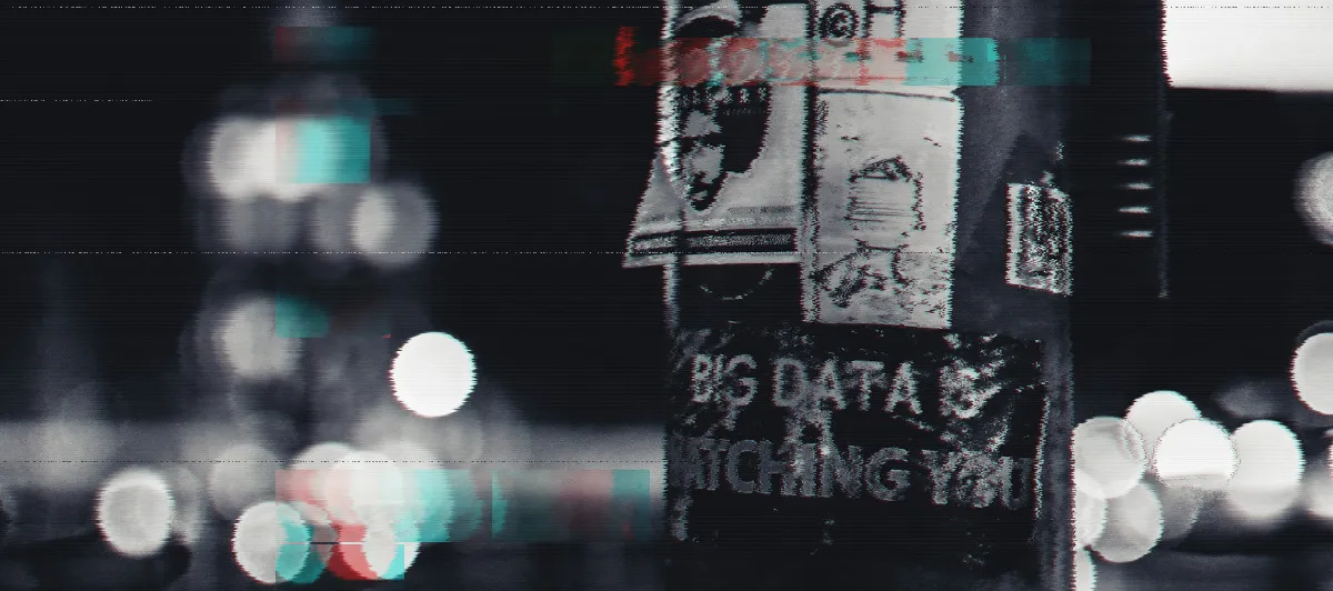 A black lightpole in a city, with a lot of stickers on it. One of them says Big Data is Watching You.