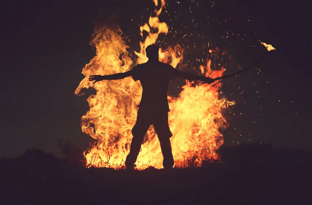 A photo of a person's dark silhouette against a tall fire in the night.
