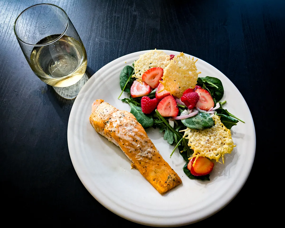 Baked salmon with a berry salad and a glass of wine.