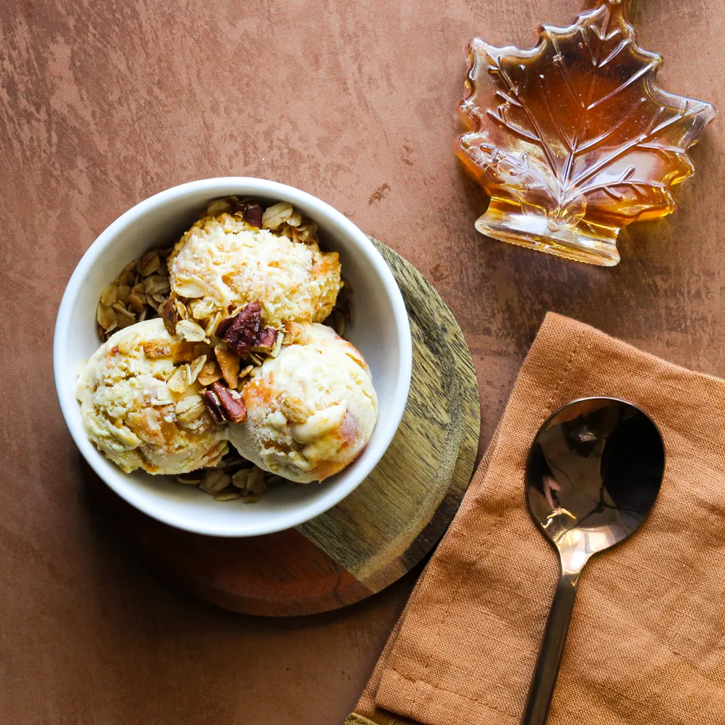 Three small scoops of peach ice cream in a bowl of granola.