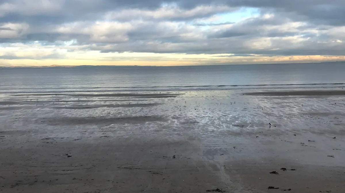 A picture of a calm sea from the beach with a cloudy sky