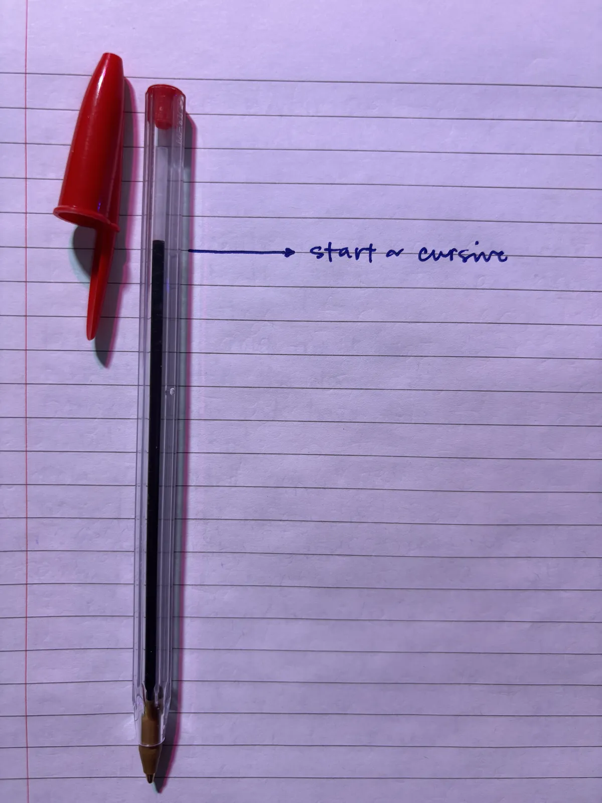 this photo has a red BIC pen on top of lined paper and it has a marker on the paper showing the starting point of the ink