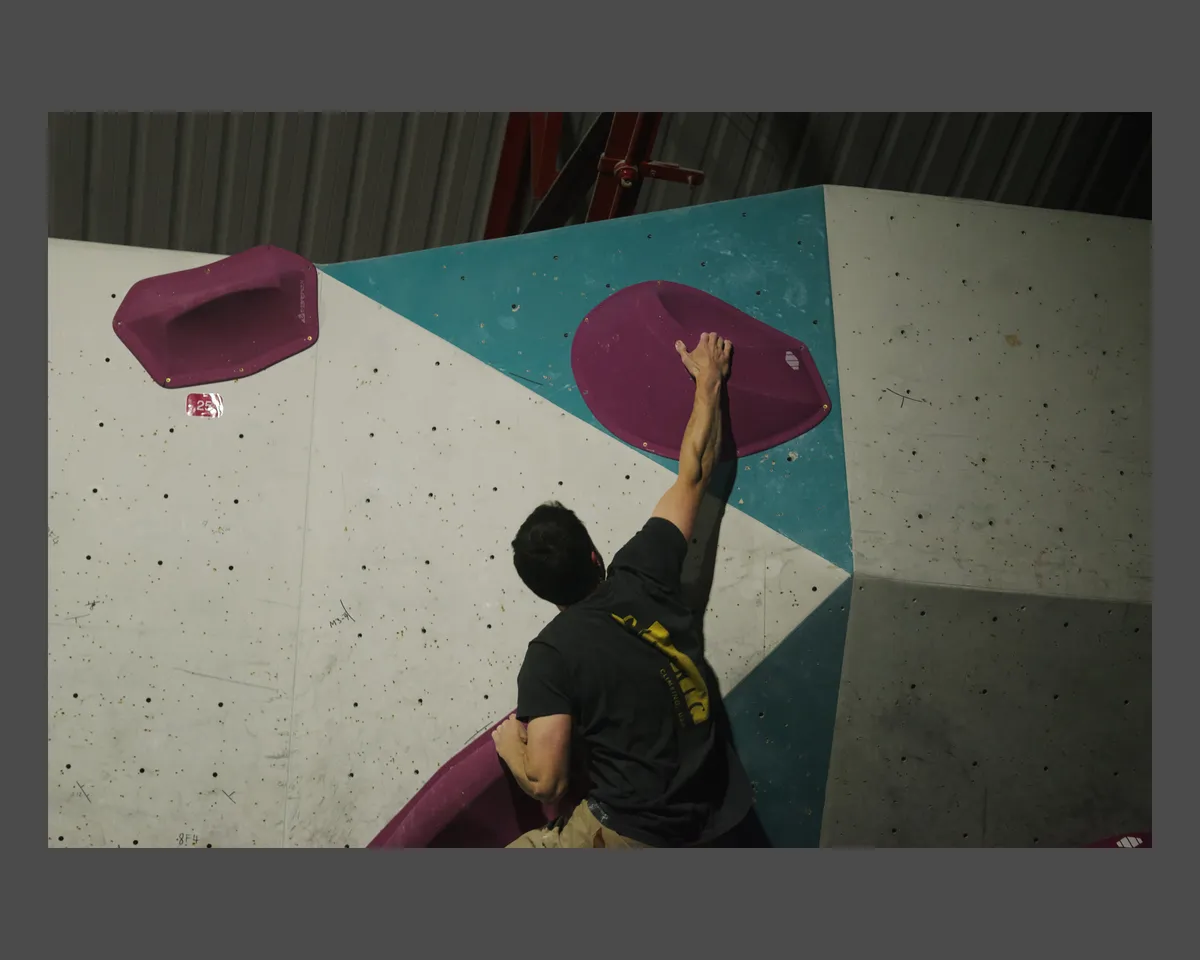 A guy reaches up to a pink sloppy boulder