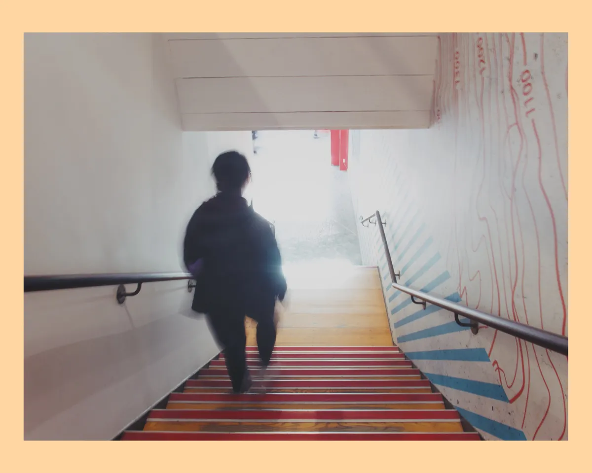 A hooded person walking down some stairs