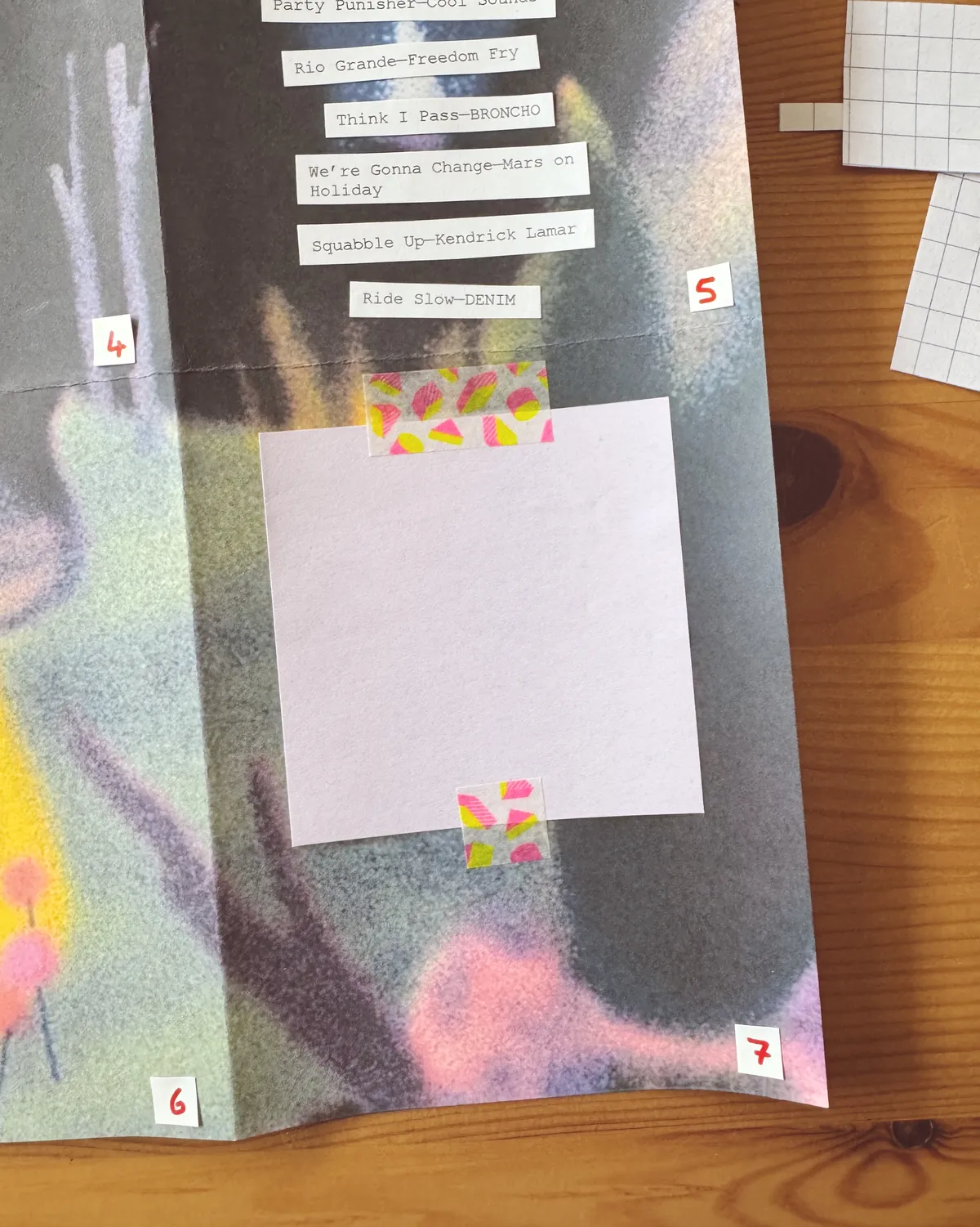 a dark background collaged zine with a sticky note attached with washi laying on a wooden table