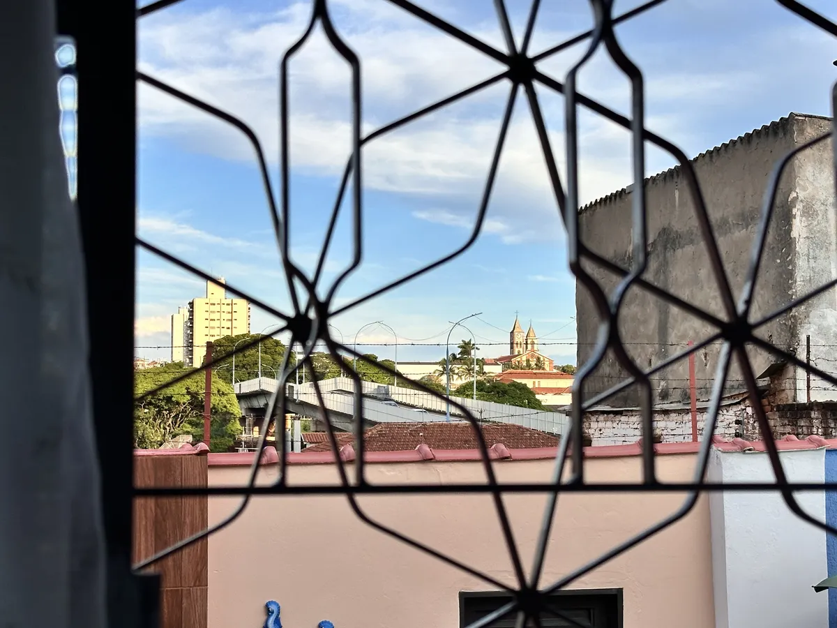 View through a window with a church in the distance. There's a railing in the window and barbed wire over a wall a few meters ahead.