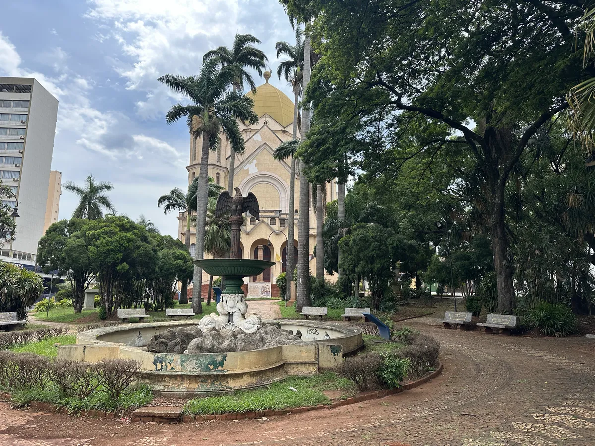 A rundown square with lots of trees and a church in the background.