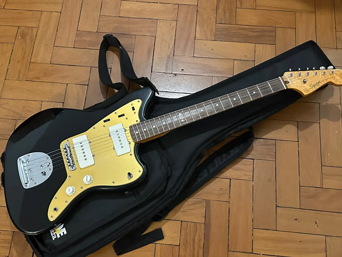 A black Squier Jazzmaster with a golden annodized pickguard.
