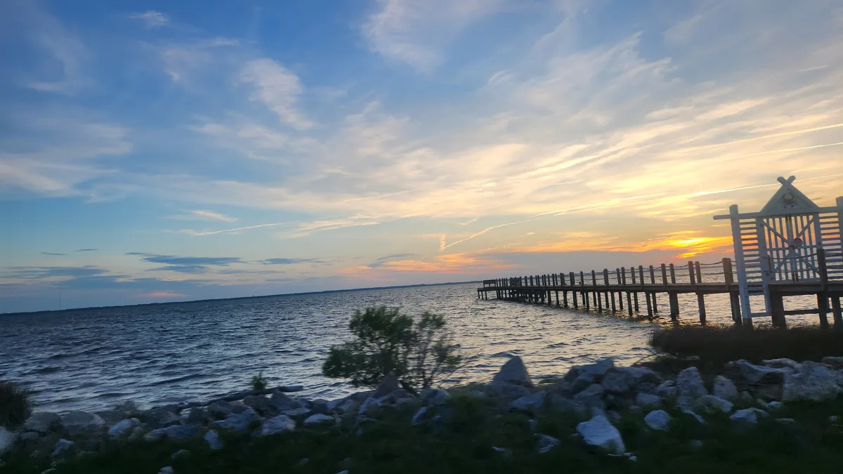 Pier extending out over grey water with early sunset in the distance
