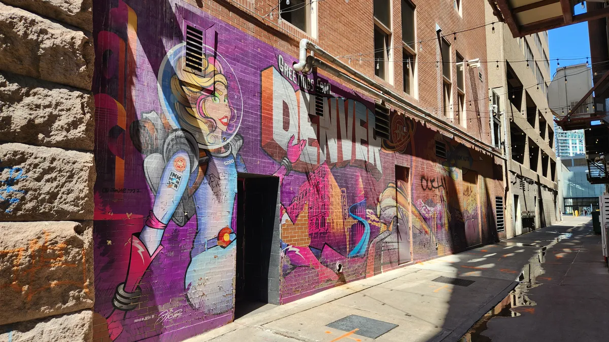 The word DENVER painted like a space postcard on the side of a building in an alley, daytime