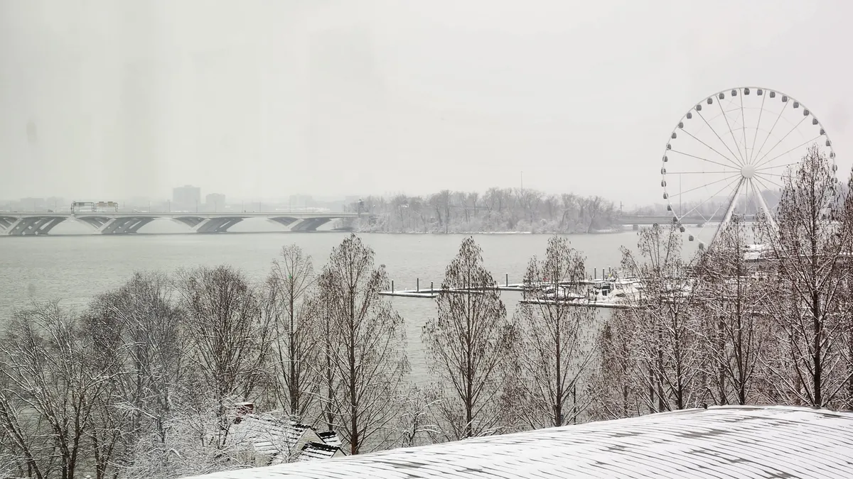 Snowy view of a Ferris wheel next to water behind a short hill