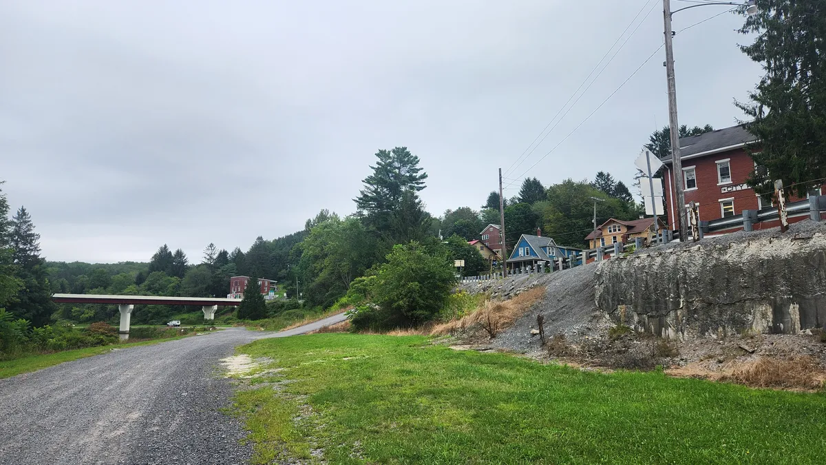 Road turning up a mountain to a row of buildings with a red bridge in the distance