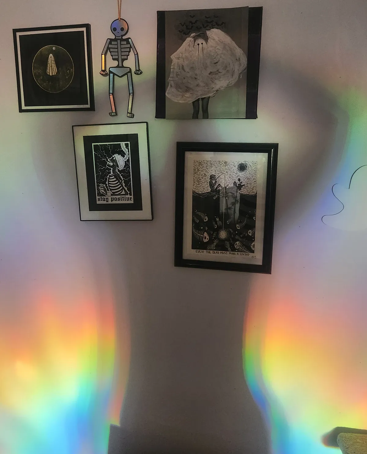 Shadow of a person with bent arms on a wall silhouetted by rainbow light, with ghost art prints displayed